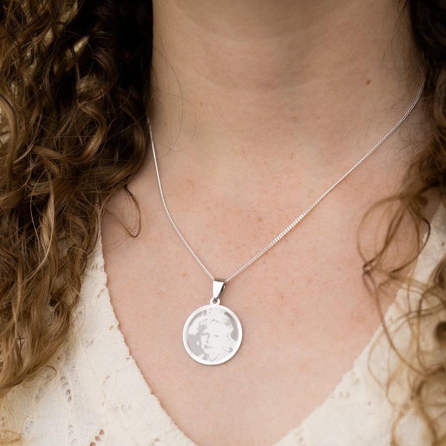 Round pendant necklace A beautiful rhodium pendant engraved with a personalized photo hanging from a silver chain around a person's neck.