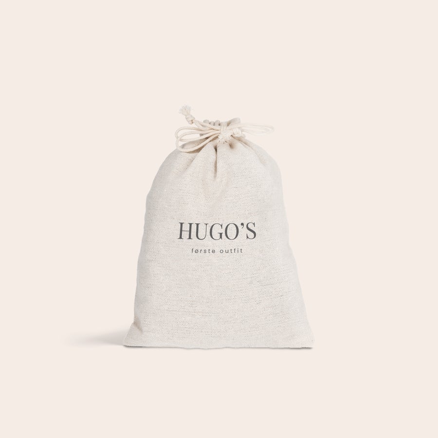 Gavepose i stof Beige gavepose i stof med sort tryk Hugo's første outfit og snørelukning, perfekt til personlige gaver.