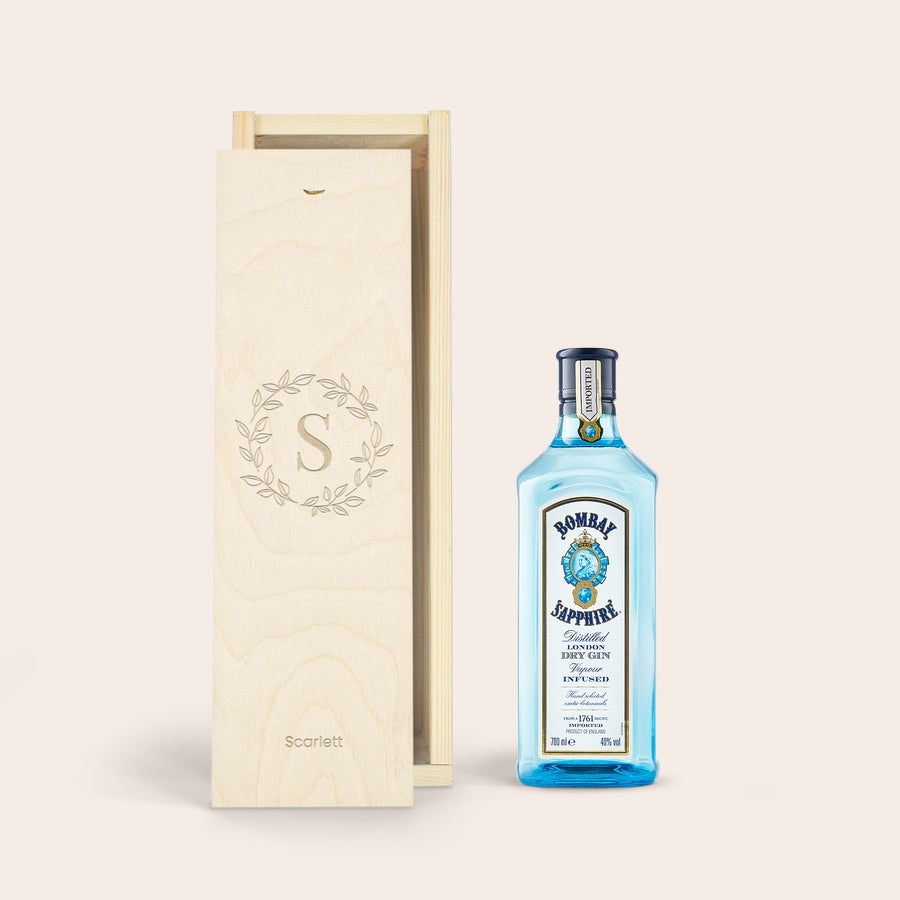 Bombay Saphire personalizado Botella de ginebra Bombay Sapphire junto a una caja de madera clara. La caja está grabada con una S mayúscula dentro de una corona de laurel y el nombre "Scarlett" debajo.