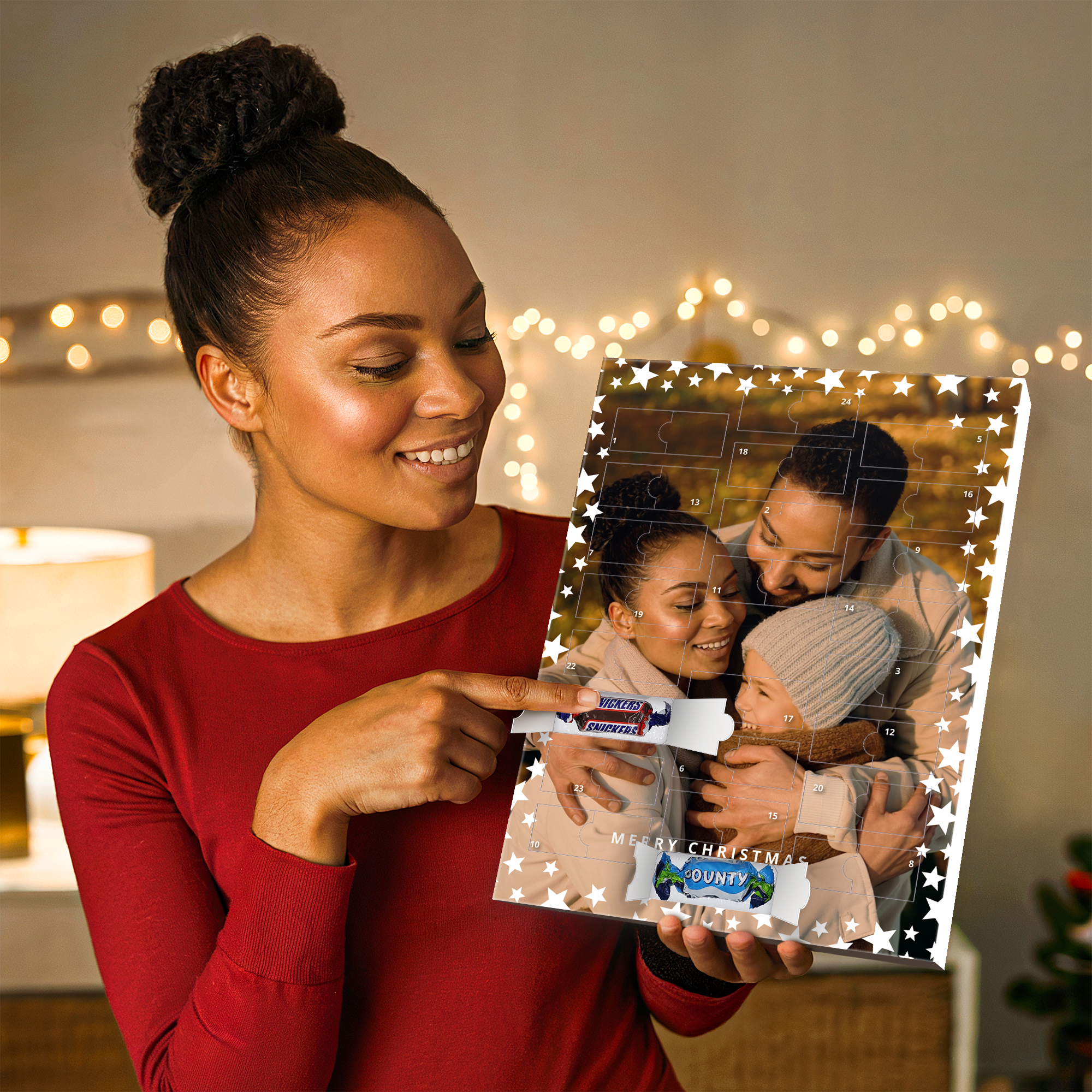Mujer sonriendo sosteniendo un calendario de Adviento personalizado con una foto familiar y un dulce Snickers, para cuenta regresiva para Navidad.