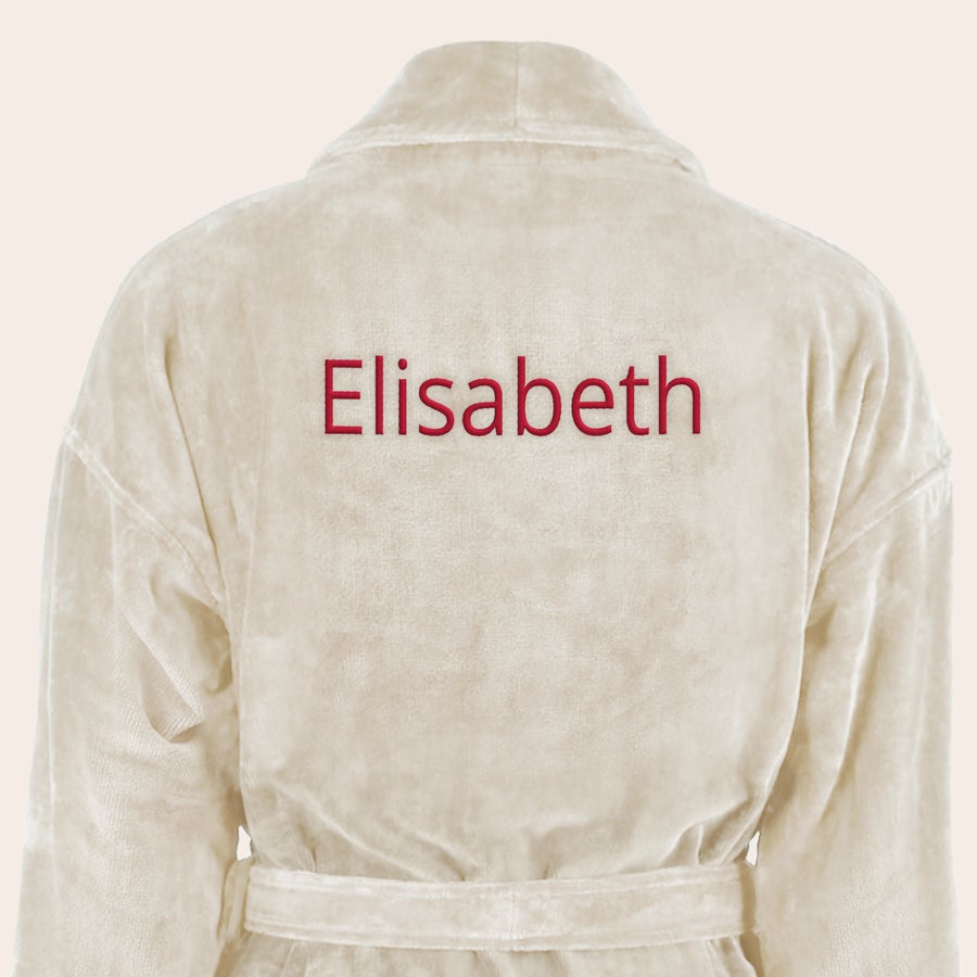Badekåpe for kvinner med navn Myk, beige badekåpe brodert med navnet "Elisabeth" i rød tråd på ryggen.