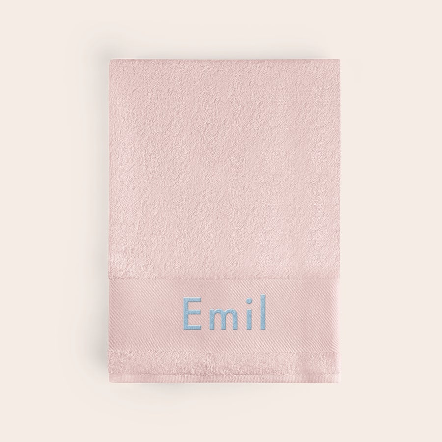 Badehåndkle med tekst Rosa badehåndkle med navnet Emil brodert i lyseblå tråd på håndklekanten for et personlig preg.