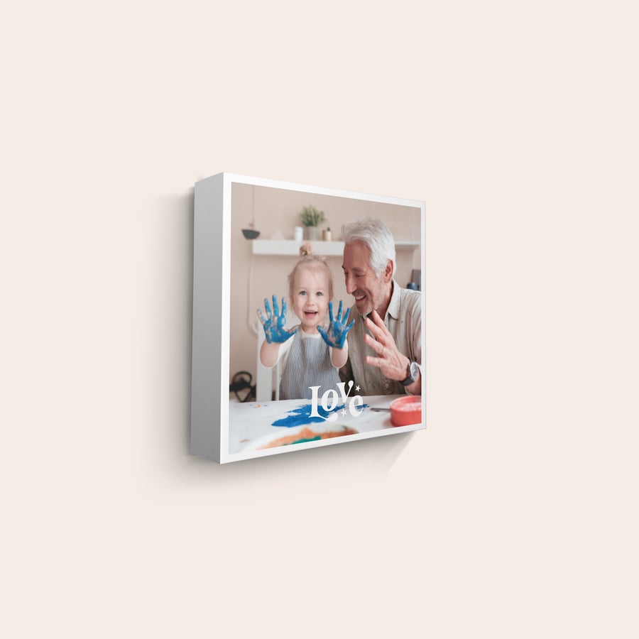 Canvas-taulu Valokuva canvas-tauluun painettuna, jossa hymyilevä lapsi ja isoisä, lapsella siniset maalit käsissään, valkoinen Love-teksti.