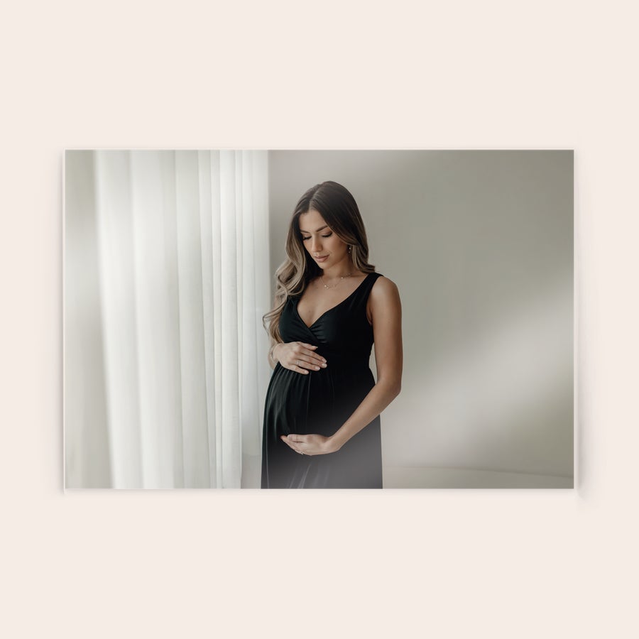 Tableau photo plexiglas Photo sur plexiglas personnalisée montrant une femme enceinte dans une robe noire posant devant une fenêtre.