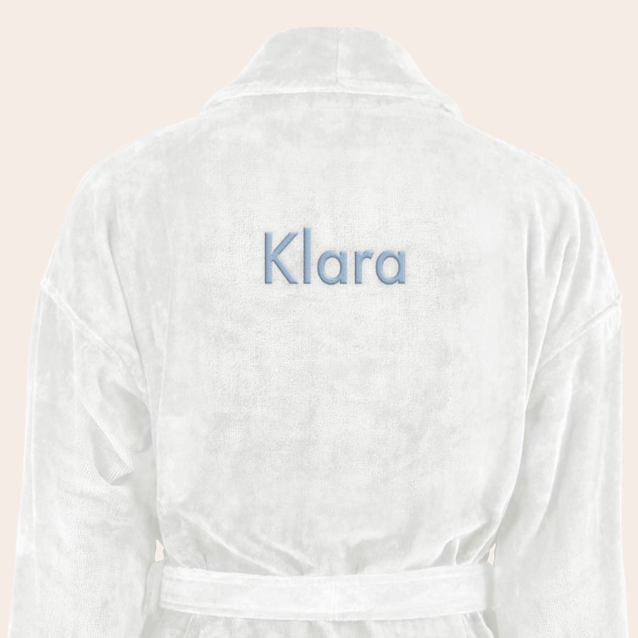 Badrock Dam med namn Vit mjuk badrock med det broderade namnet Klara i blå tråd som en personlig gåva.