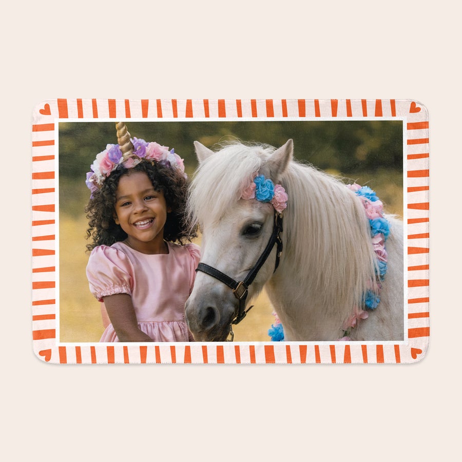 Pătură foto din lână Pătură fleece personalizată, imprimată cu fotografia unei fetițe zâmbitoare și a unui ponei alb, amândoi decorați cu flori, având o ramă albă cu dungi portocalii și inimi.
