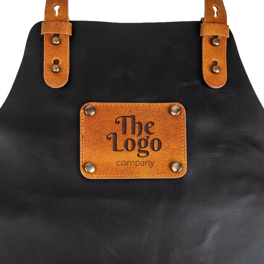 Tablier en cuir personnalisé Tablier de chef en cuir noir avec étiquette personnalisée The Logo Company, gravé au laser, fixée avec des rivets.
