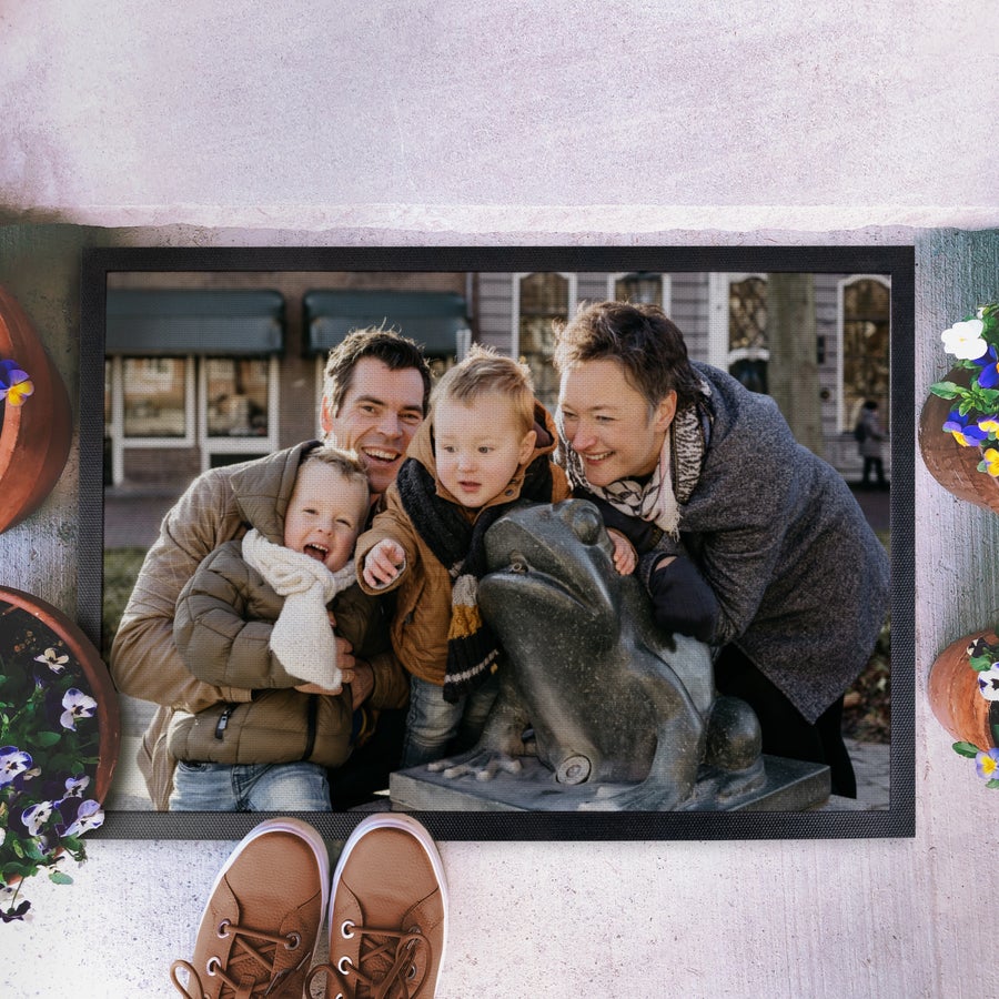 Prilagojena predpražnik Natisnjen predpražnik s fotografijo družine, ki objema figuro žabe.