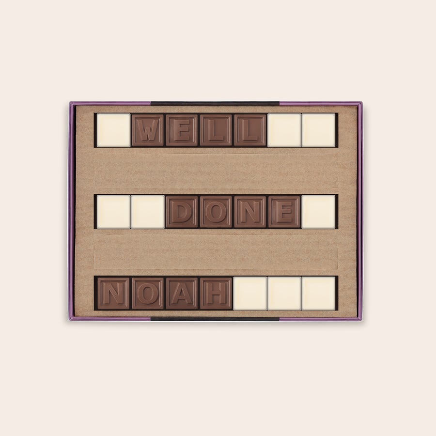 Chocotelegram Een persoonlijk chocotelegram met de tekst "WELL DONE NOAH" in melk- en witte chocolade blokjes, gepresenteerd in een cadeauverpakking.