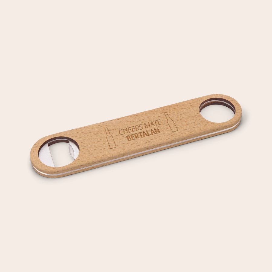 Gravírozott egyedi fa sörnyitó Fából készült, gravírozott sörnyitó "Cheers Mate Bertalan" szöveggel, két sörösüveg grafikával, fém nyitóval a végén.