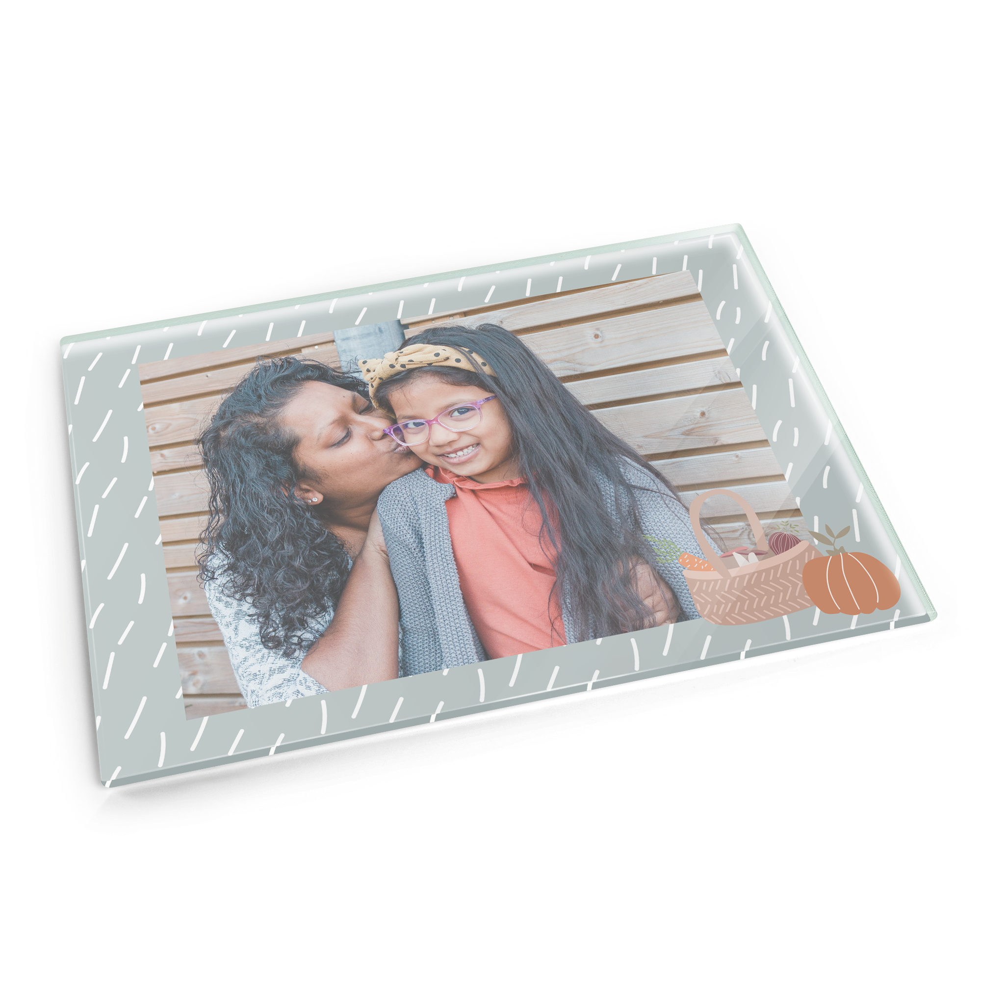 A glass chopping board personalized with a photo of a woman kissing a girl and a basket with vegetables