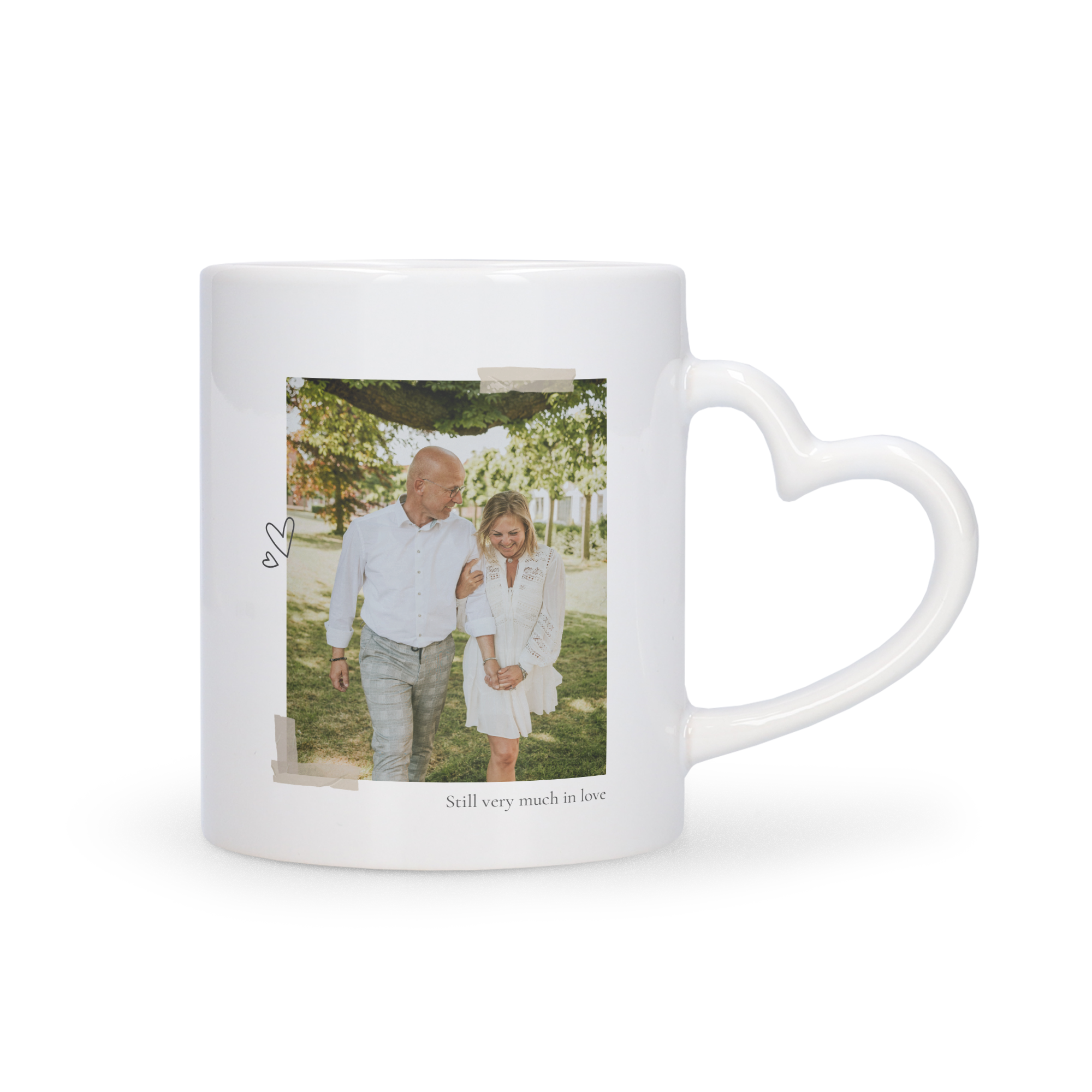 Taza blanca con asa en forma de corazón, impresa con foto de pareja y el texto "Still very much in love", para regalar.