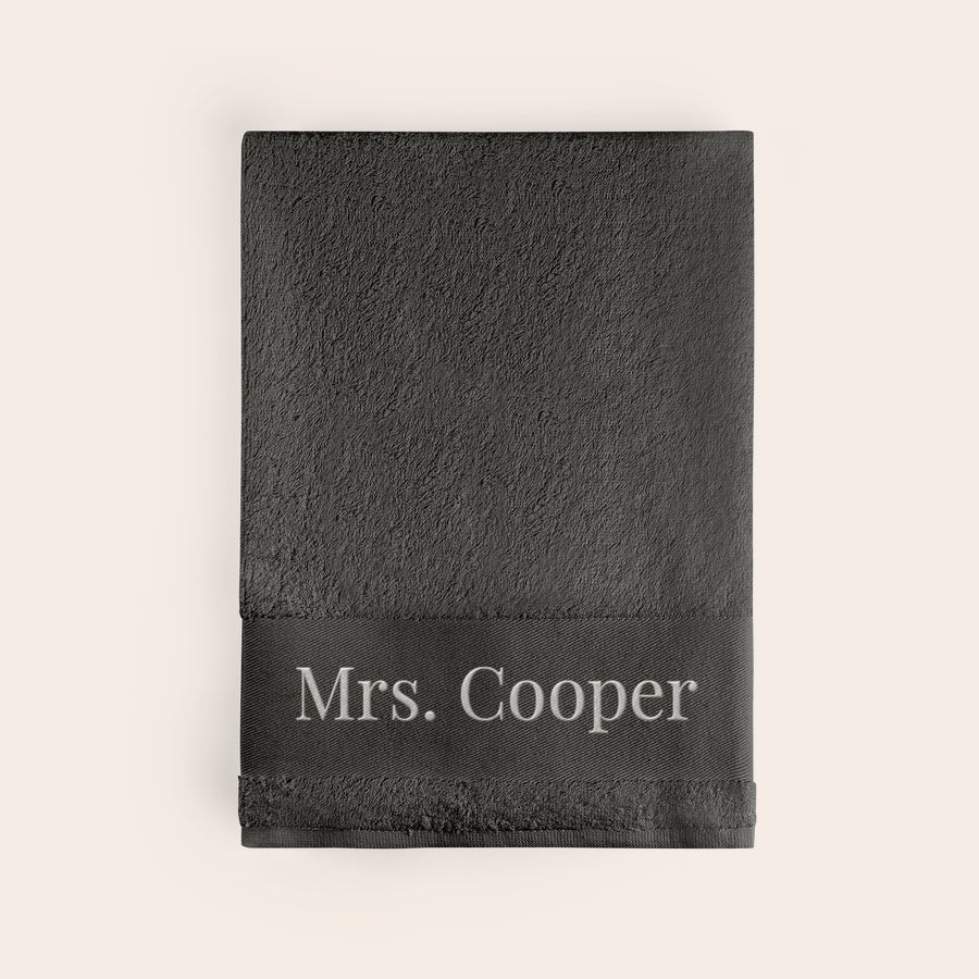 Toalla de baño con texto Toalla de baño personalizada en color antracita con el nombre "Mrs. Cooper" bordado en blanco.
