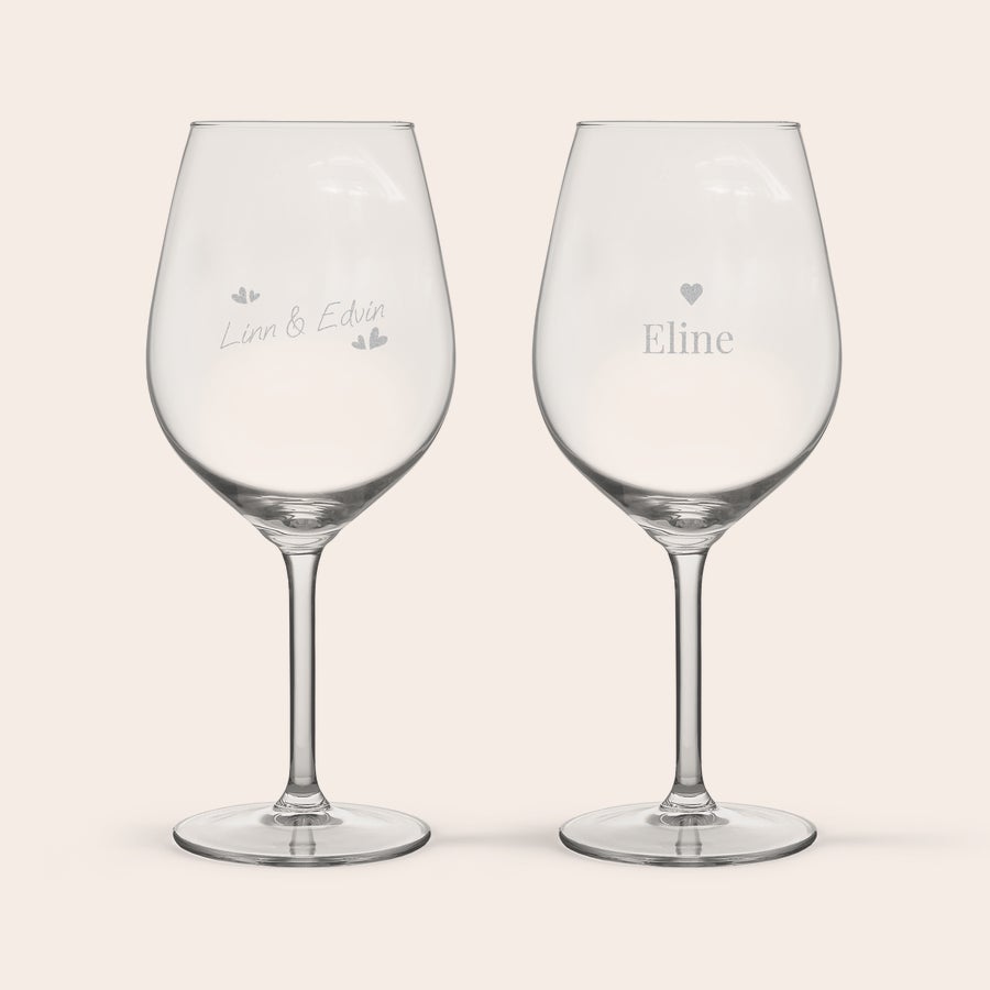 Röd Vinglas Två vinglas graverade med namn och illustrationer, det ena med "Linn & Edvin" och små hjärtan, det andra med "Eline" och ett hjärta.