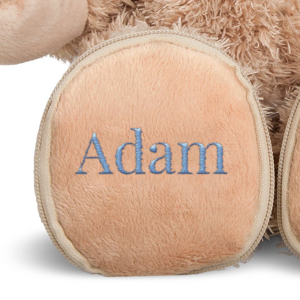 Ours en peluche personnalisé couleur crème avec le prénom Adam brodé en bleu sur la patte