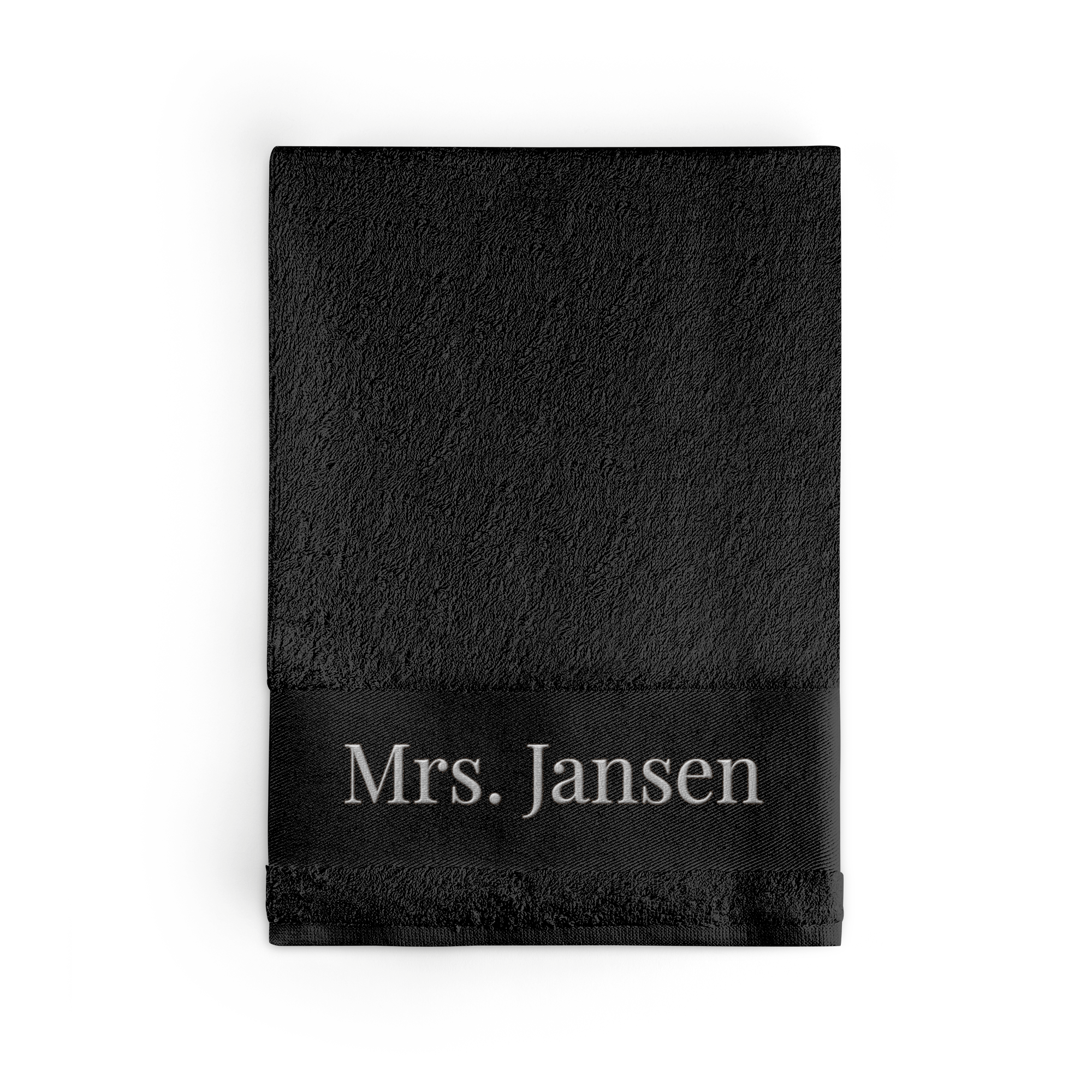 Zwart badlaken met naam "Mrs. Jansen", geborduurd in wit garen
