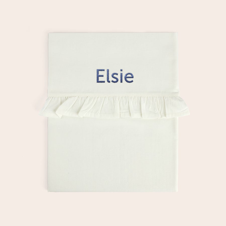 Sábana para cuna bordada - Borde con volantes Sábana de moisés blanca con el nombre Elsie bordado en azul y borde de volantes.