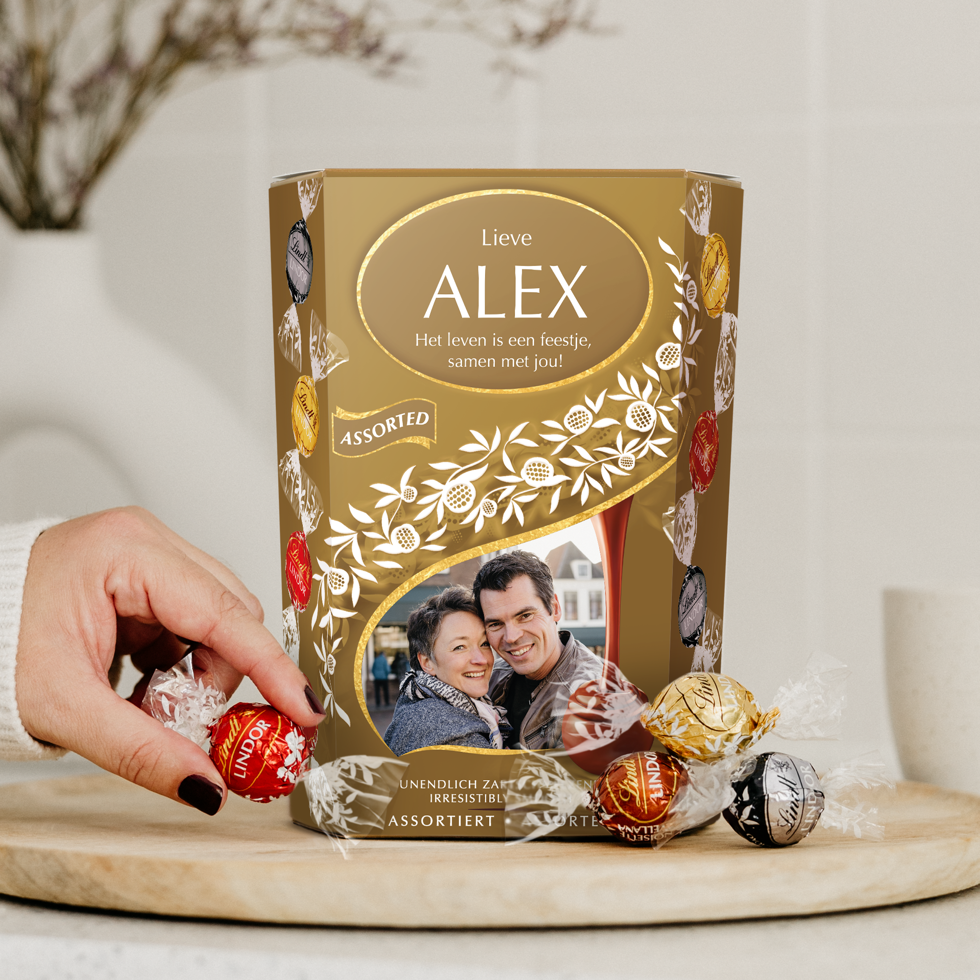 Gepersonaliseerde Lindt chocolade giftbox met een gedrukte foto van een stel, de naam "Alex" en tekst "Het leven is een feestje, samen met jou!". De Lindt Chocolade giftbox is een perfect cadeau voor chocoladeliefhebbers.