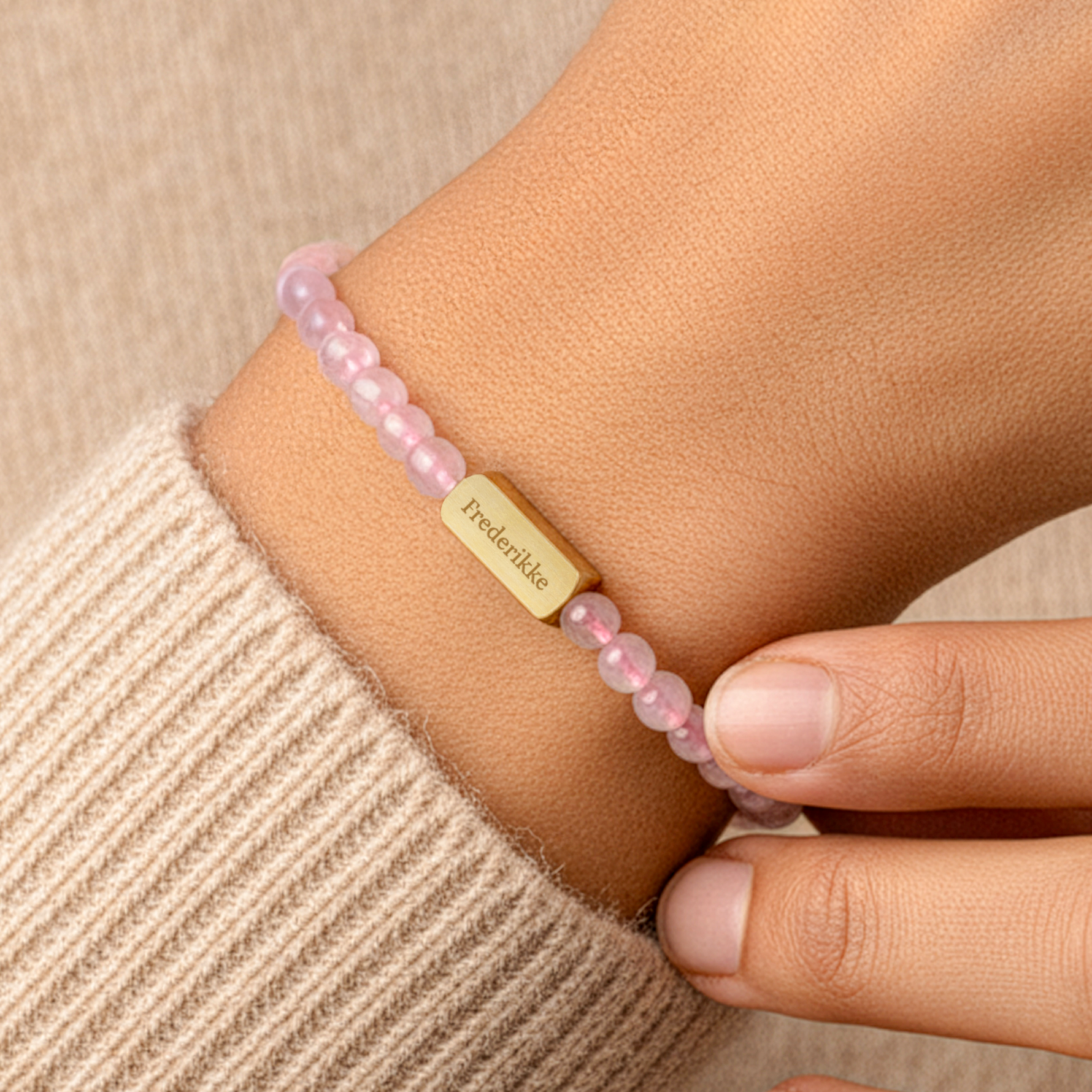 Armbånd med graveret rosenkvarts - M - 4 mm - Guld, med 'Frederikke' graveret på den guldfarvede plade, båret på et håndled.