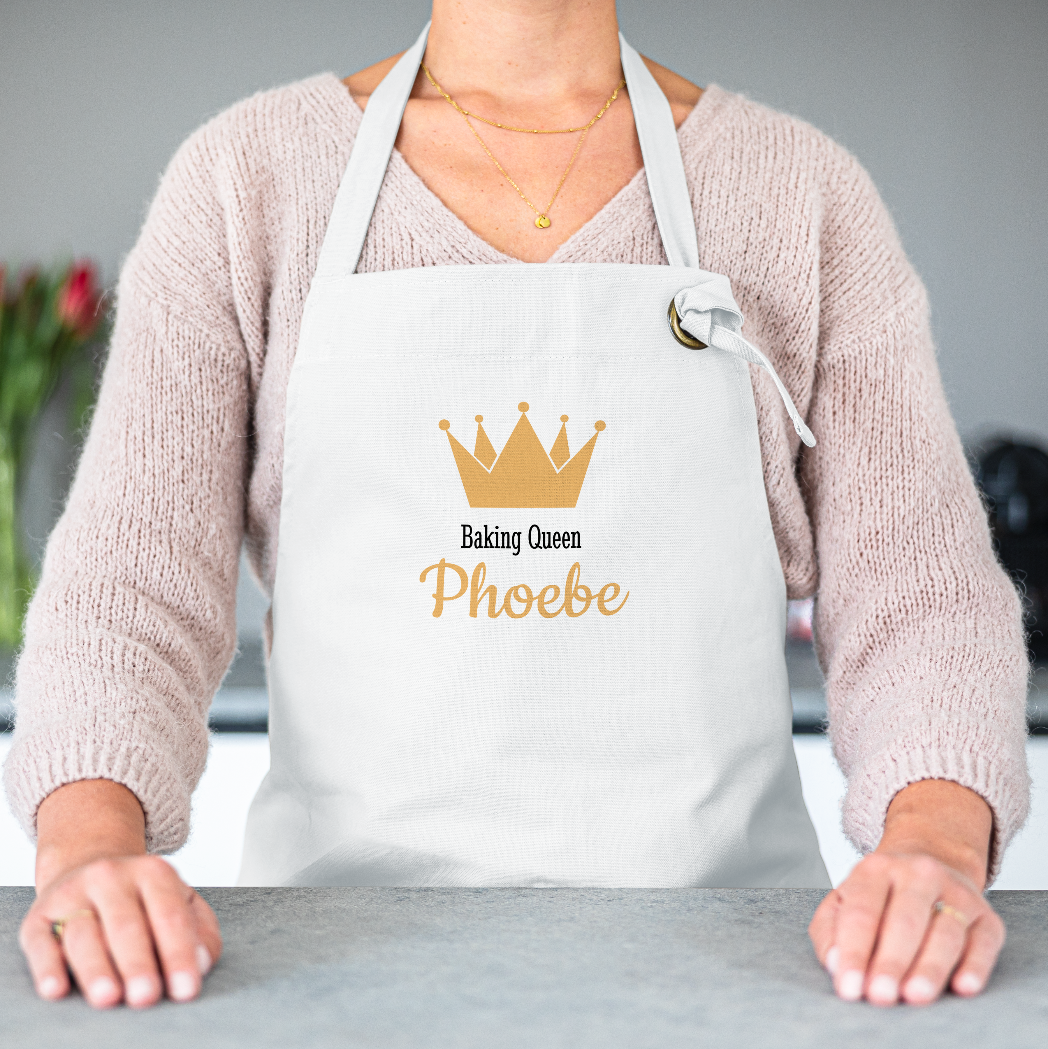 Hvit kjøkkenforkle med trykt gullkrone, teksten "Baking Queen" og navnet "Phoebe".