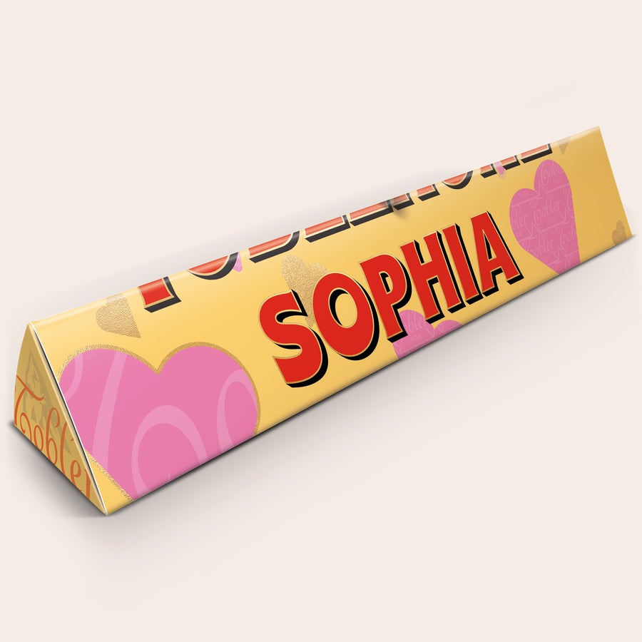 Toblerone XXL Személyre szabott XXL Toblerone csokoládé sárga csomagolásban, "SOPHIA" névvel és rózsaszín szívekkel nyomtatva