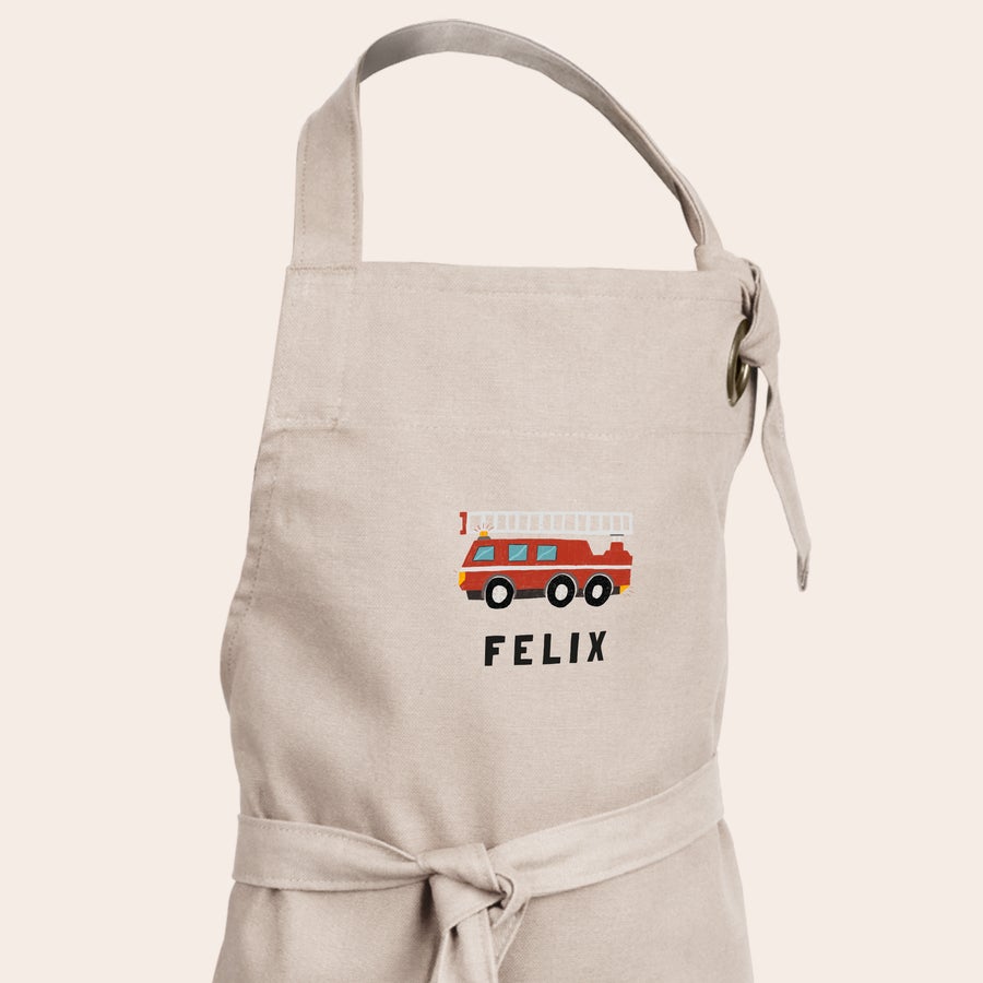 Kinderschürze personalisiert Beige Kinderschürze mit rotem Feuerwehrauto-Aufdruck und dem Namen Felix, personalisiert bedruckt