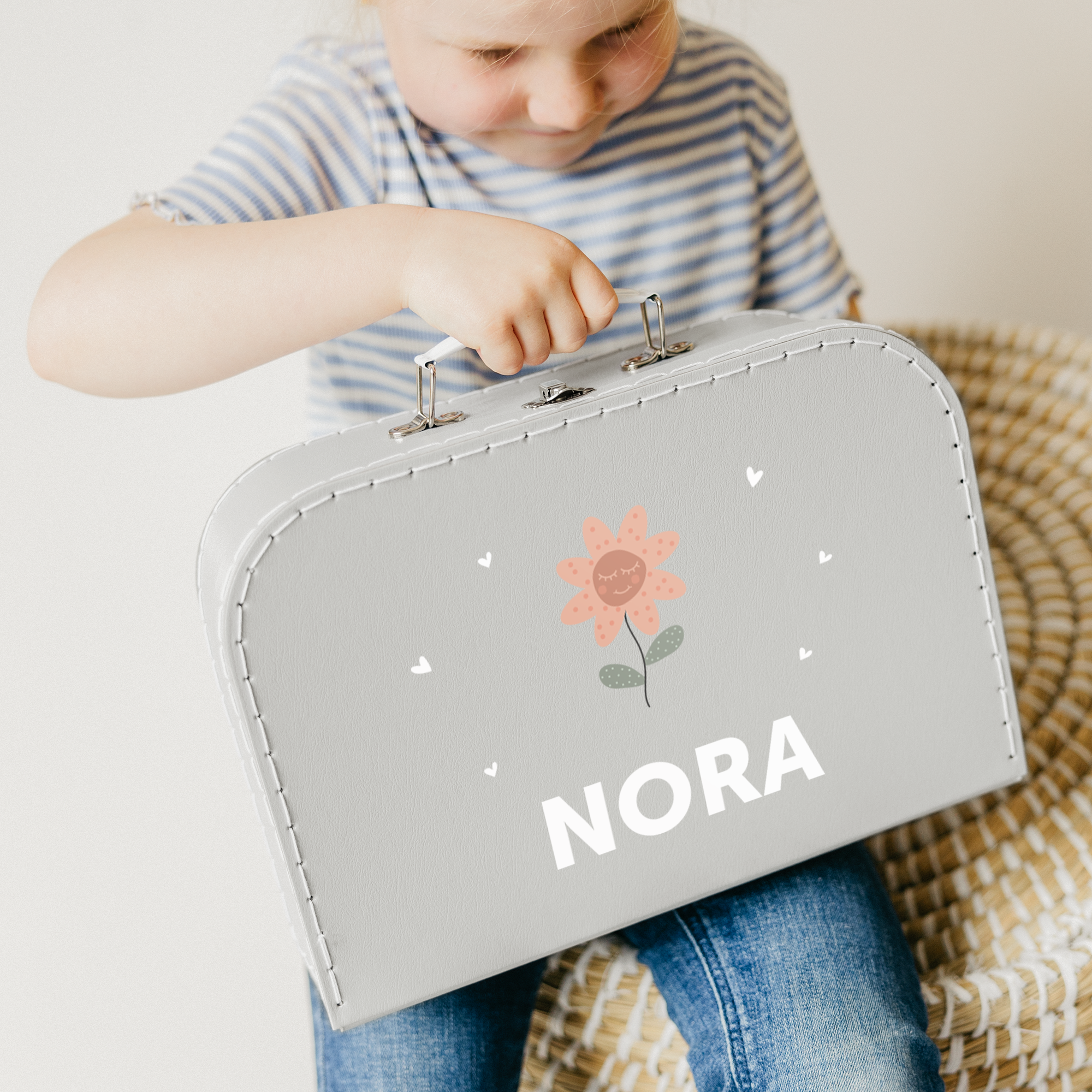 Kind met een bedrukte kinderkoffer in grijs met een bloemdesign en de naam NORA.