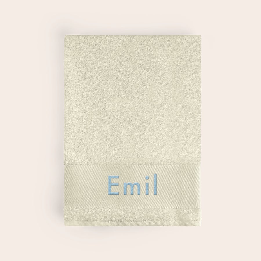 Badehåndkle med tekst Supermykt beige badehåndkle brodert med navnet Emil i lyseblått. Få ditt eget badehåndkle brodert med navn.