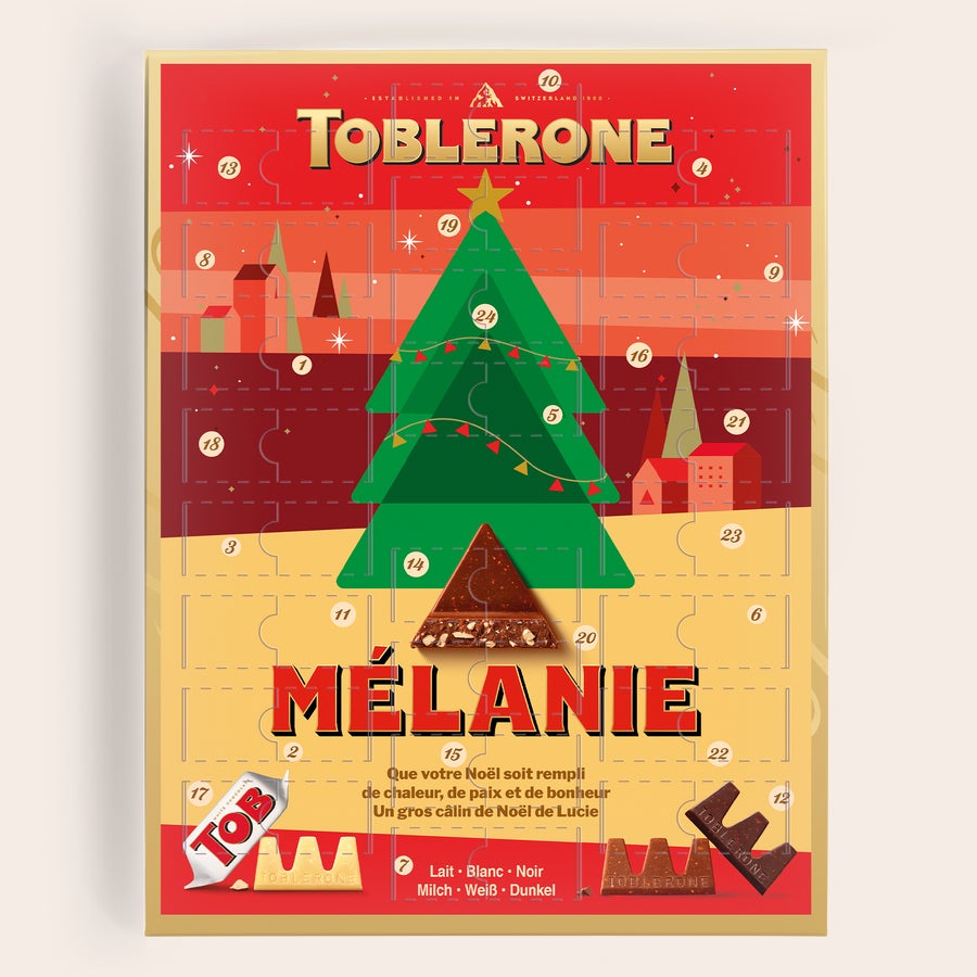Calendrier de l'avent Toblerone  2025 Calendrier de l'Avent Toblerone personnalisé avec le prénom Mélanie, un sapin de Noël et le message imprimé Que votre Noël soit rempli de chaleur.