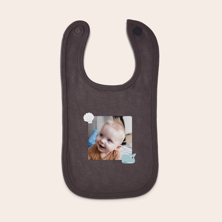 Personalised baby bib Personalized bib with a photo of a smiling baby, a white seashell, and a blue whale printed on a dark brown bib.