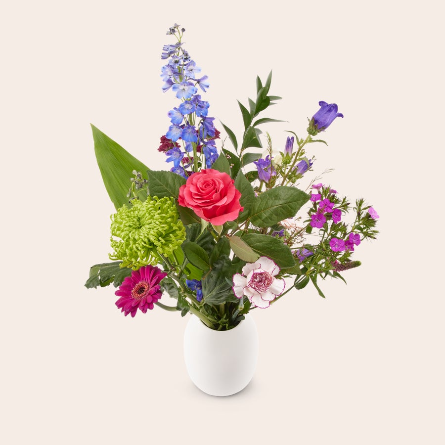 Bloemen - Natuurlijk plukboeket Natuurlijk plukboeket met roze roos, paarse bloemen en groen blad in een witte vaas, geleverd met een gratis cadeaukaartje.