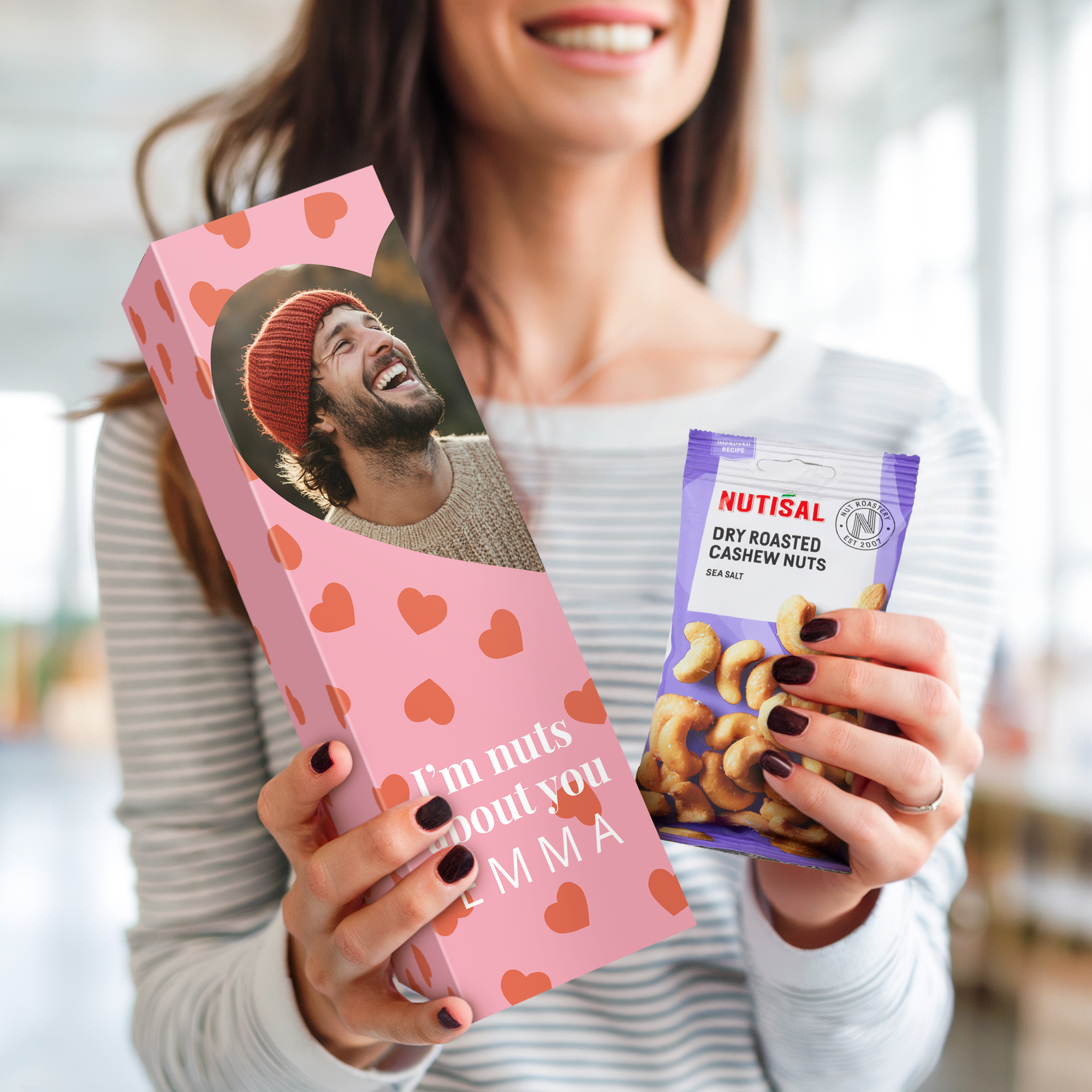 Rožnata personalizirana darilna škatla z natisnjeno fotografijo in napisom I'm nuts about you EMMA, poleg nje vrečka indijskih oreščkov.