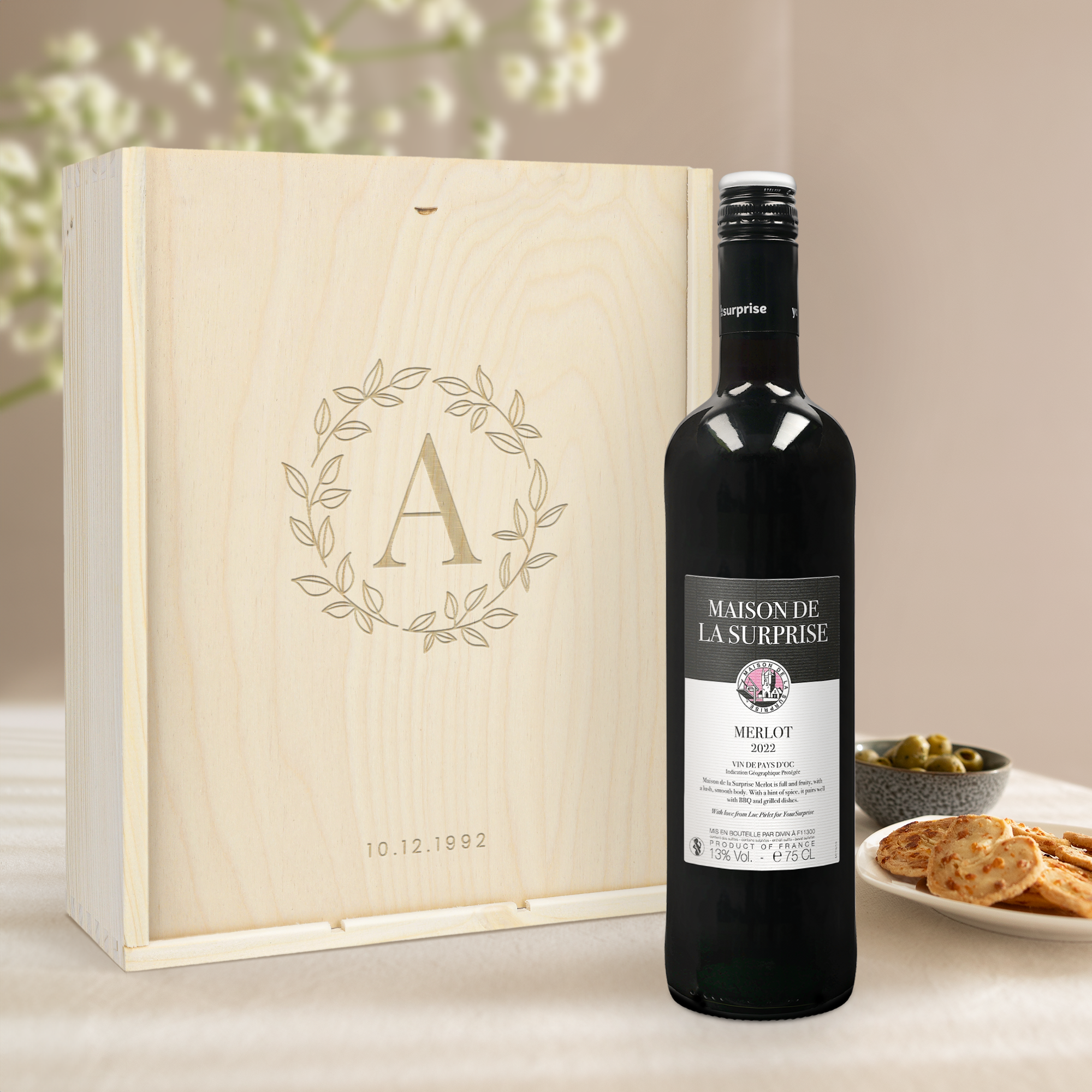 Vinpaket Maison de la Surprise i graverad vinlåda med initialen A i krans och datum 10.12.1992, samt en flaska rött Merlotvin.