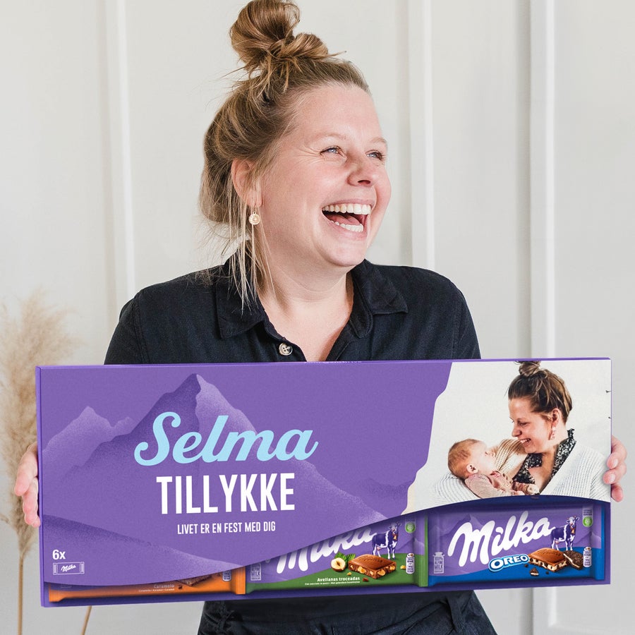 Personlig Mega Milka med navn og billede En glad kvinde holder en Personlig Mega Milka Chokolade med eget design - 6 plader, med navn "Selma", en personlig hilsen og eget foto.