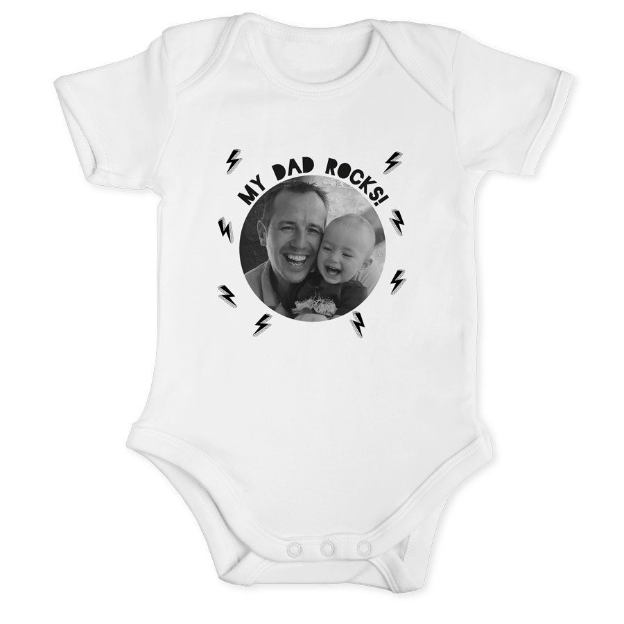 Hvit babybody med trykt bilde av far og barn, samt teksten "My Dad Rocks!". Feire pappas første farsdag med et personlig tema.