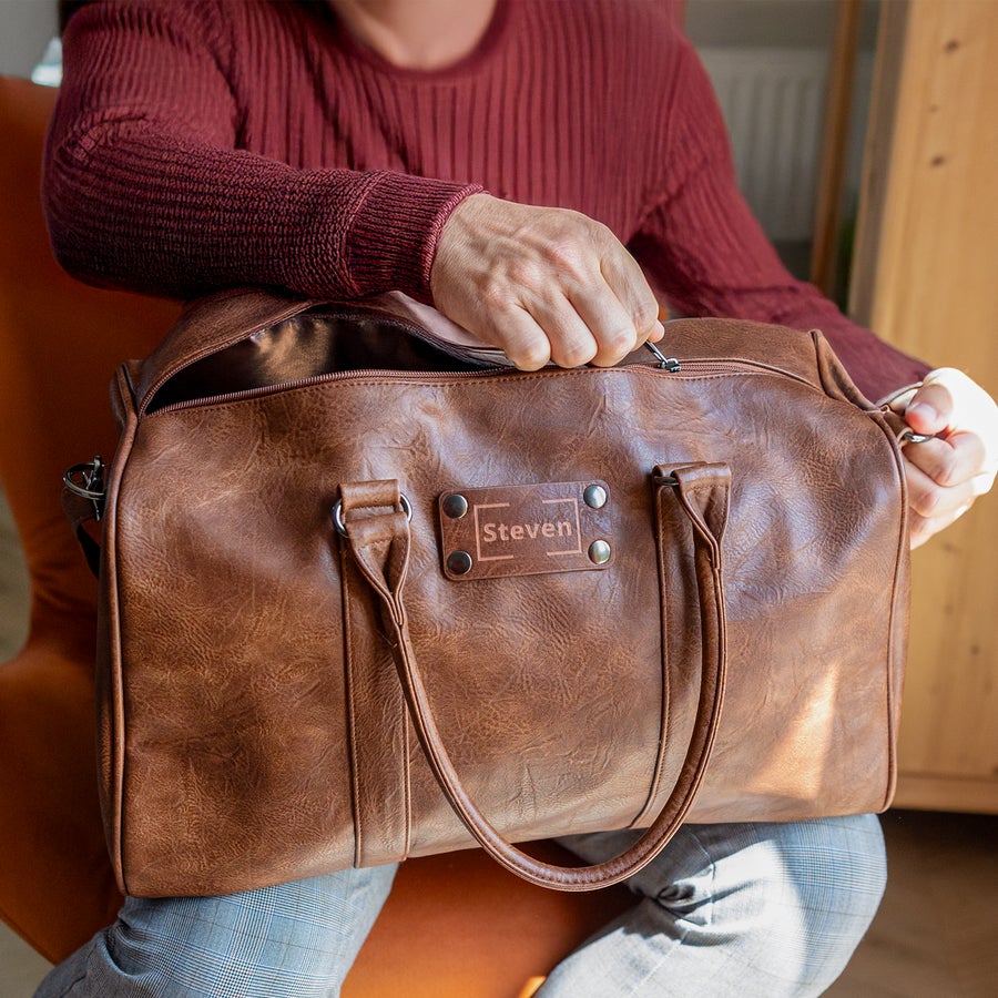 Personalisierte Reisetasche Braune personalisierte Reisetasche aus Kunstleder, mit dem Namen Steven auf einem Etikett graviert.