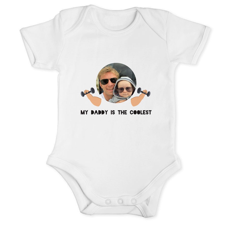 Hvit babybody med trykt bilde av far og barn, samt tekst Feire pappas første farsdag med et personlig tema.