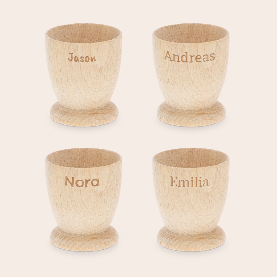 Eierbecher personalisiert Vier personalisierte Eierbecher aus hellem Buchenholz, graviert mit den Namen Jason, Andreas, Nora und Emilia, um das Frühstück unvergesslich zu machen