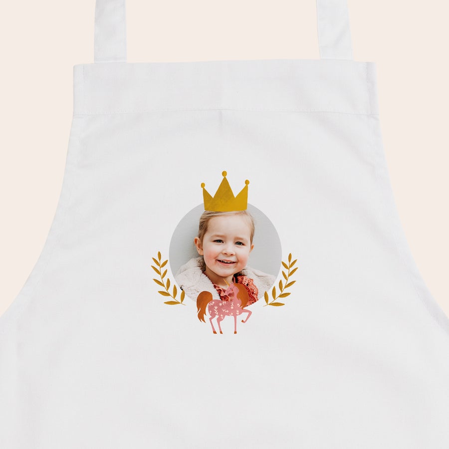 Kinderschürze personalisiert Weiße Kinderschürze mit Foto eines Mädchens, goldener Krone und Einhorn bedruckt.
