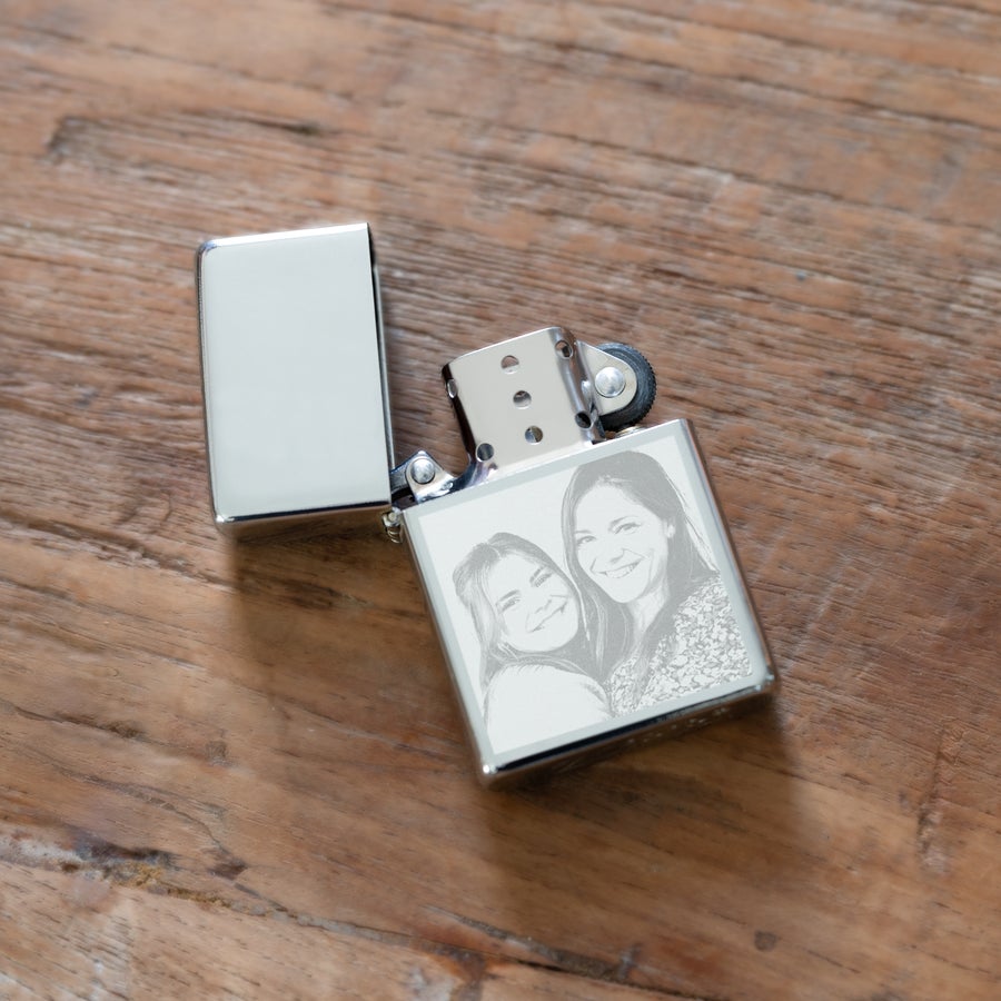 Isqueiro gravado Isqueiro prateado aberto com foto de duas mulheres sorrindo gravada, sobre uma superfície de madeira. Transforme memórias em uma chama de elegância com nosso isqueiro de foto gravada