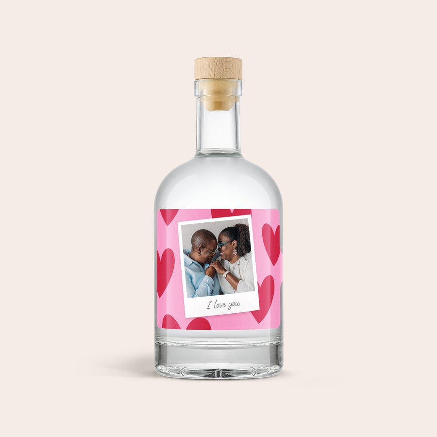 Personlig YourSurprise Gin En utsökt flaska gin med personlig etikett. Etiketten är tryckt med ett foto av ett par och texten I love you på en rosa bakgrund med röda hjärtan.