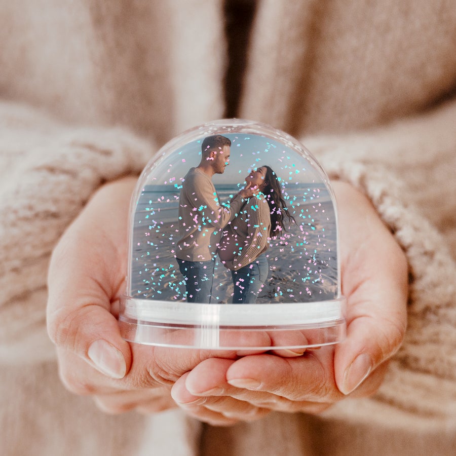 Sneeuwbol met foto Een gepersonaliseerde glitter sneeuwbol met een foto van een stel op het strand, in handen gehouden