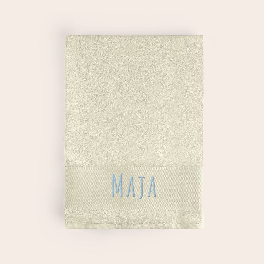 Badehåndkle med tekst Beige badehåndkle brodert med navnet "Maja" i lyseblå tråd. Få dette supermyke badehåndkleet brodert med navn!