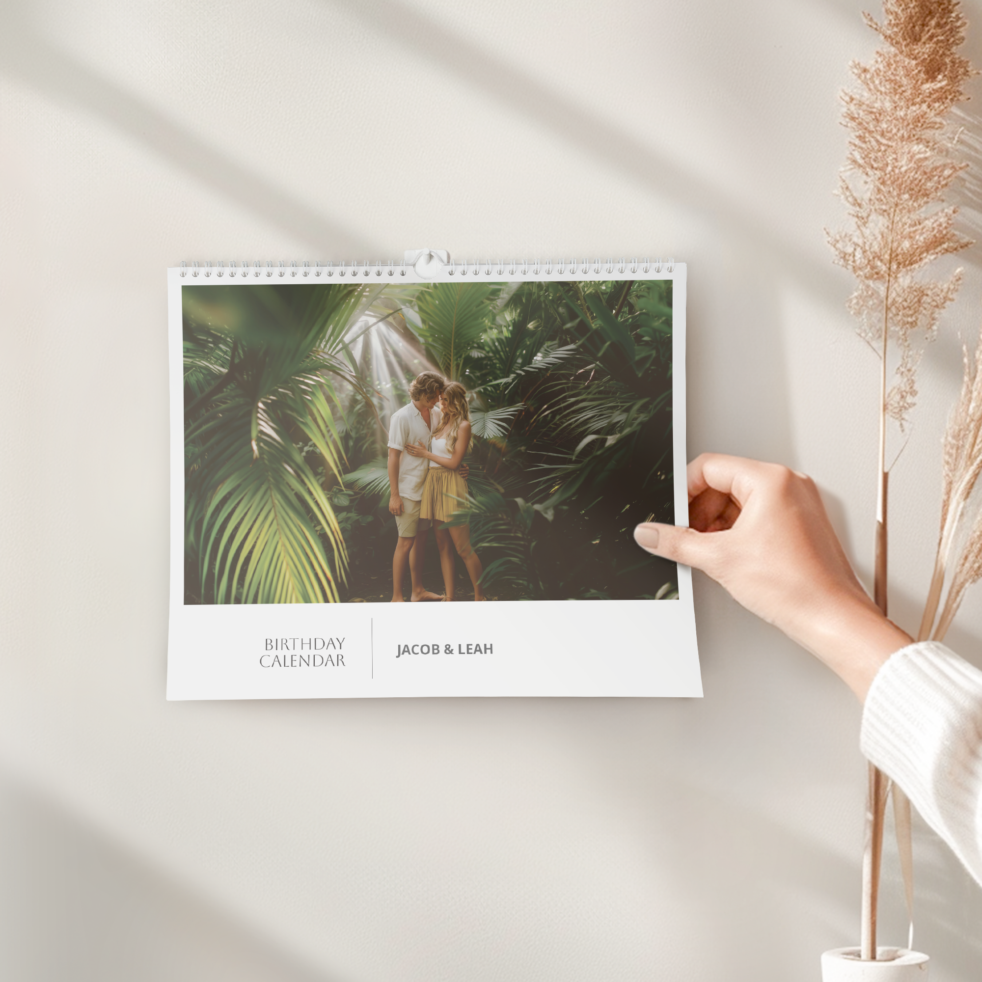 A hand adjusting a personalised birthday calendar, printed with a photo of a couple and the names Jacob & Leah.
