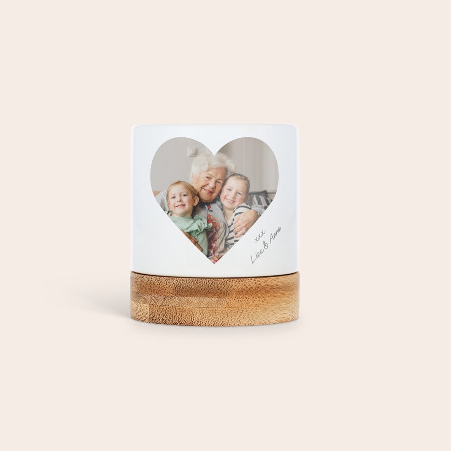 Bloempot met foto Gepersonaliseerde witte bloempot met bamboe onderzetter, bedrukt met een hartvormige foto van een oma en twee kinderen en handgeschreven tekst Geef hun groen een persoonlijk tintje.