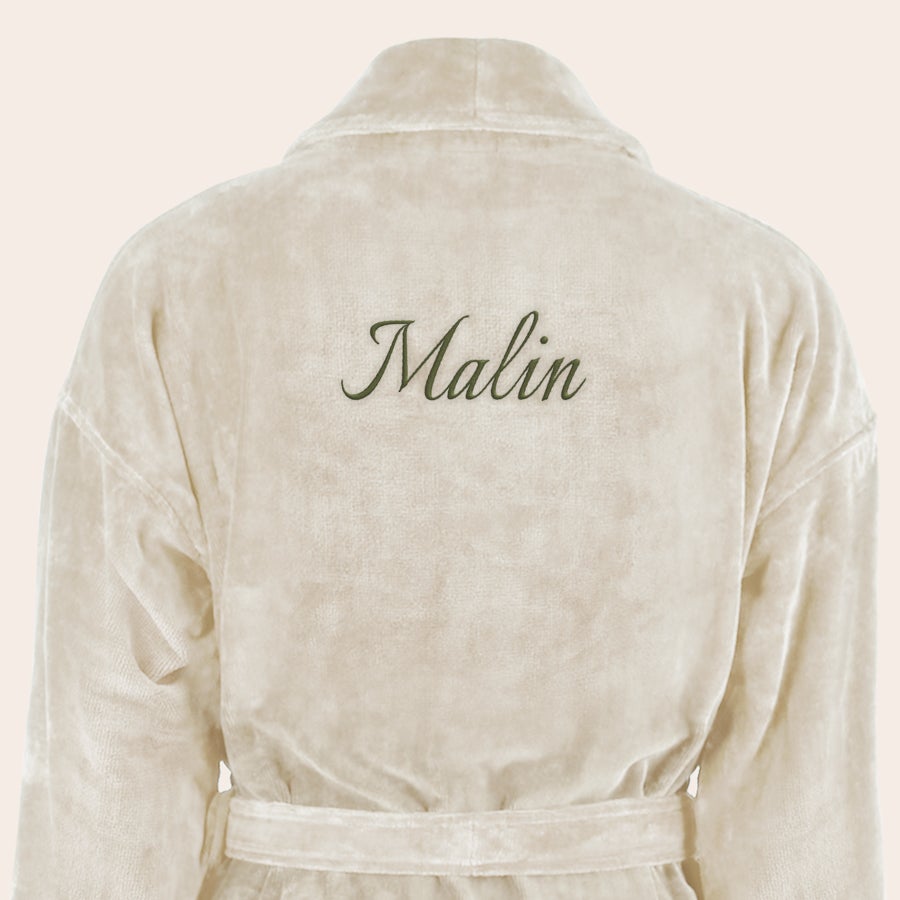 Badekåpe for kvinner med navn Myk, beige badekåpe brodert med navnet "Malin" i grønn skrift på ryggen.