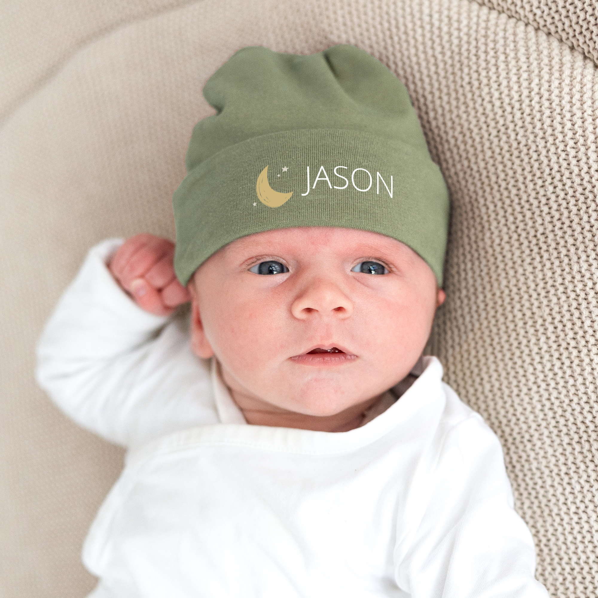Een baby draagt een groen babymutsje bedrukt met de naam Jason en een gele maan met sterren