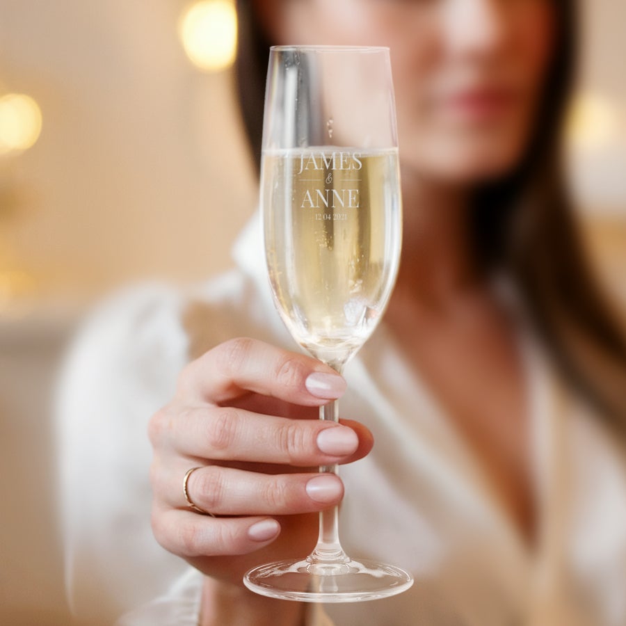 Sektgläser mit Gravur Hand hält ein Sektglas mit Namen "James & Anne" und Datum "12.04.2021" eingraviert, gefüllt mit Sekt
