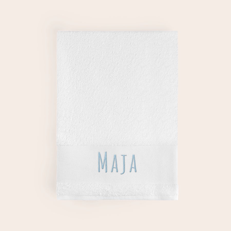 Håndkle med tekst Mykt hvitt håndkle brodert med navnet "MAJA" i lyseblått.