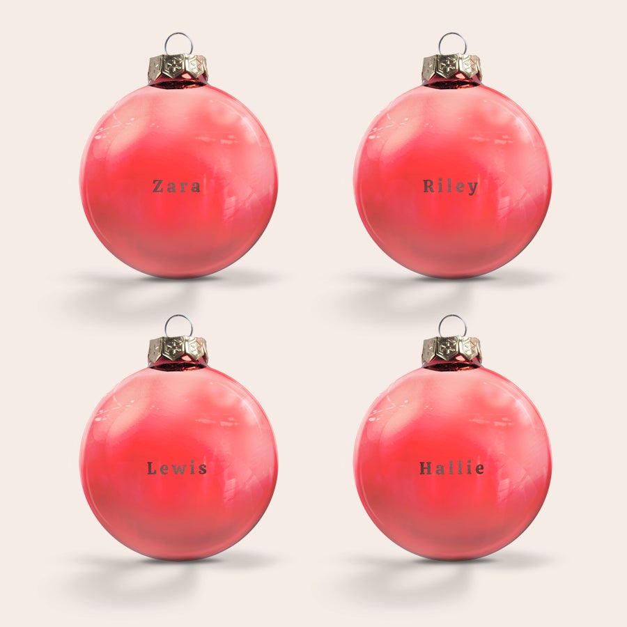 Glass bauble with name Four red glass Christmas baubles, each engraved with a different name. The baubles are Zara, Riley, Lewis, and Hallie.
